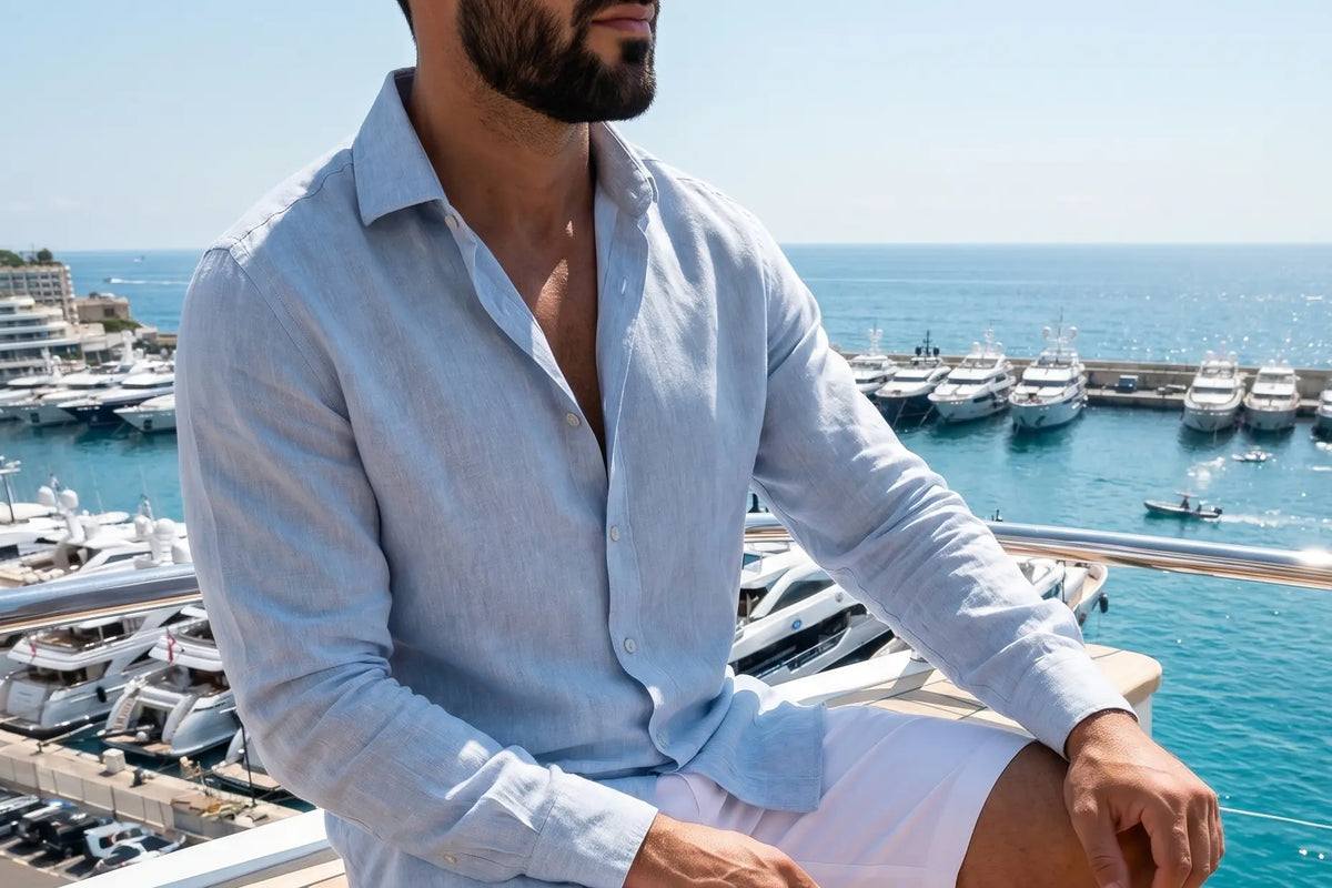 Homme assis en chemise en lin bleu clair, épaule et manche visibles, devant un port au soleil