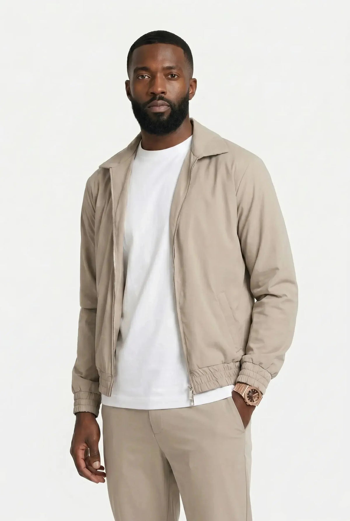 Homme en blouson zippé et pantalon assortis couleur sable, portés sur un t-shirt blanc, sur fond clair uni